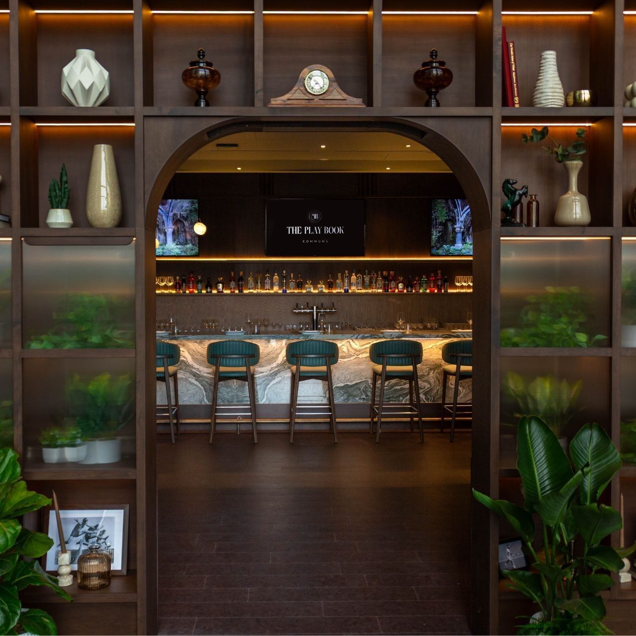 Hotel Bar at Hotel X Toronto, with green stools placed by a marble counter under an arched, plant-filled doorway