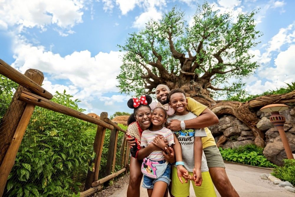 A mom and dad embrace their kids standing in front of the Tree of Life at Disney's Animal Kingdom theme park.