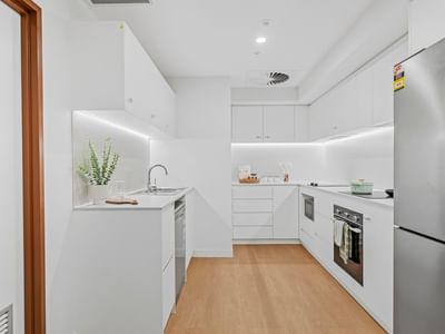 White modern kitchen with refrigerator, oven, and wooden floors at UniLodge Brisbane City.