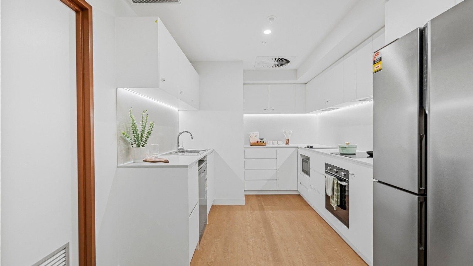 White modern kitchen with refrigerator, oven, and wooden floors at UniLodge Brisbane City.