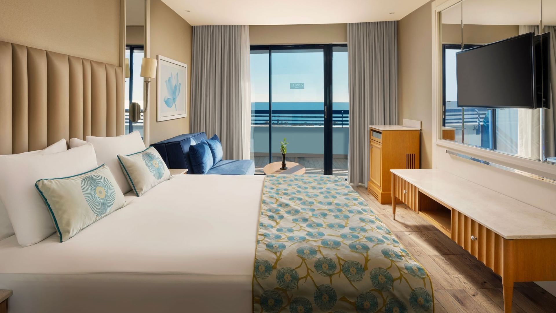 Colonel Suite with a large bed featuring blue floral bedding, a sofa, a TV, and a desk at Titanic Deluxe Lara