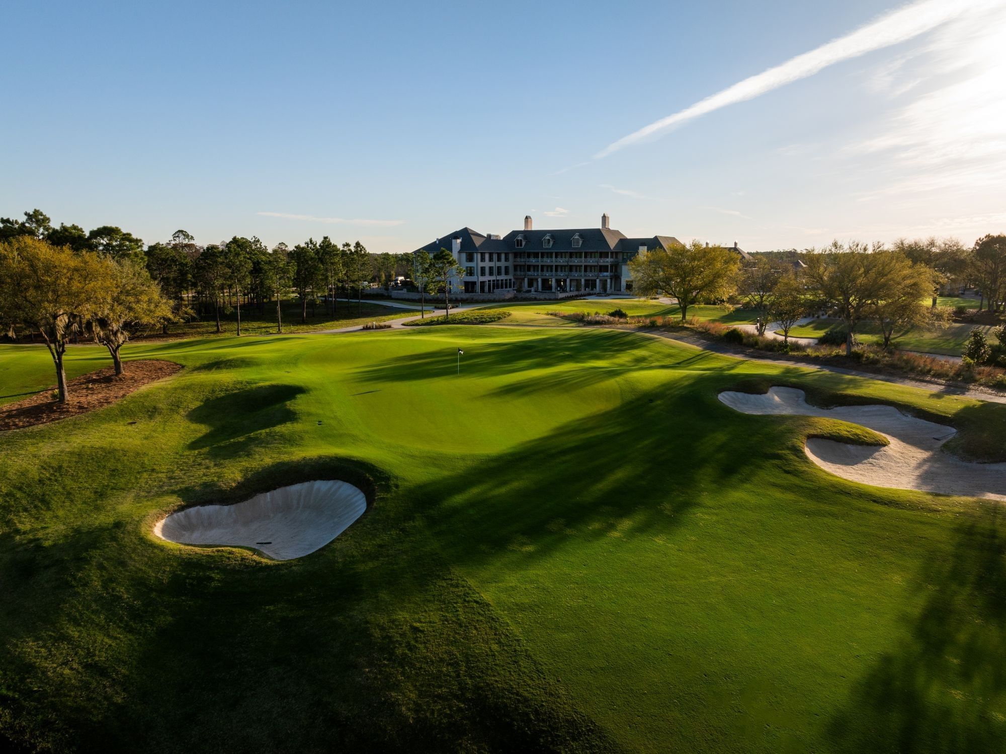 Aerial view of golf course with bunkers and a large hotel in the background at Camp Creek Inn.