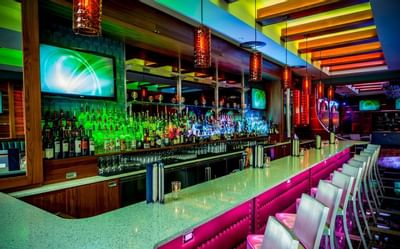 Vibrant bar counter illuminated with neon lights and lined with chairs in Harborside Bar and Lounge at Harborside Inn Boston