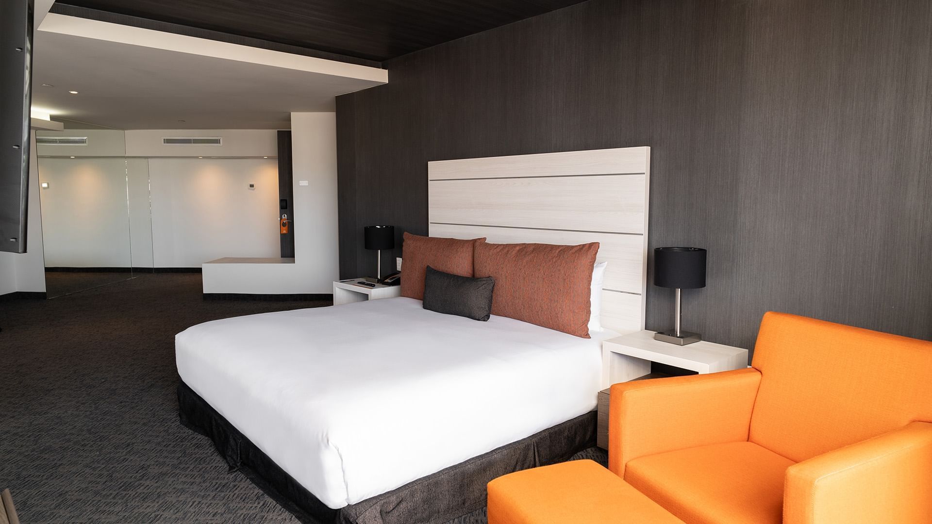 King Presidential Suite with a light wood headboard, black lamps, and an orange armchair at the Real Inn Tijuana