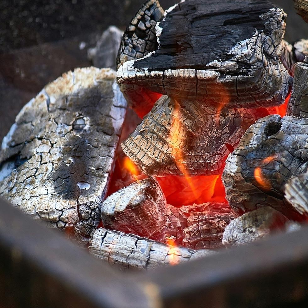 Legna nera carbonizzata e legno in fiamme in un braciere con fiamme arancioni.