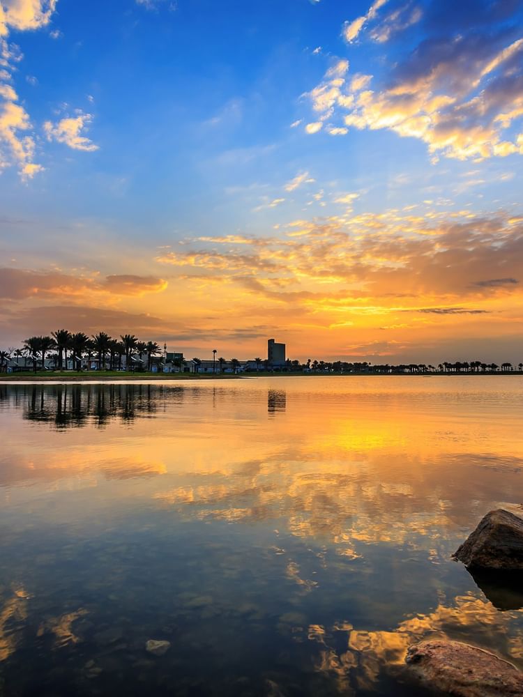 Dammam with Scenic sunset over a calm lake and palm trees along the shore and rocks near Warwick Hotels & Resort