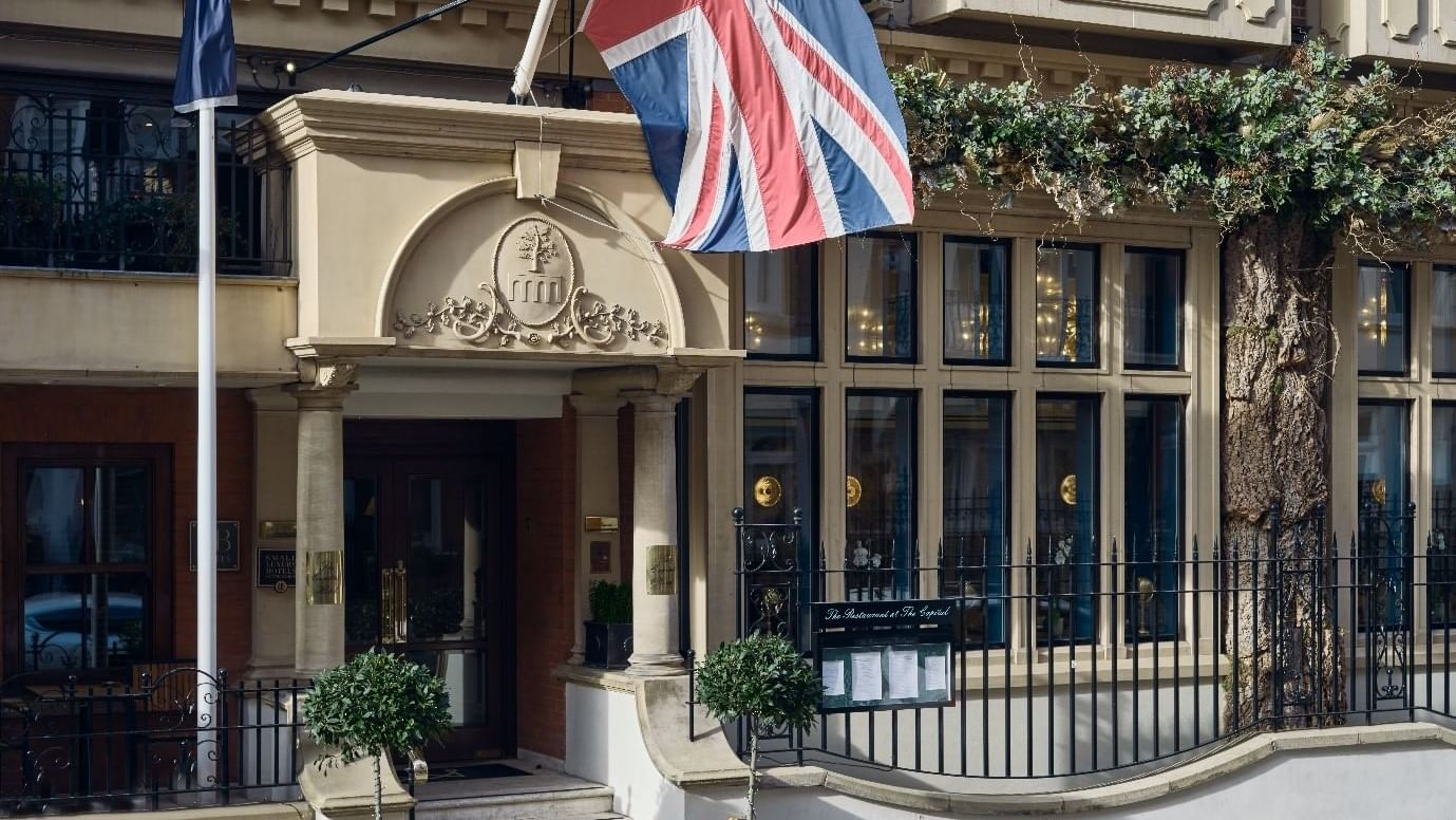 The entrance of a Capital Hotel London adorned with a British flag and surrounded by greenery