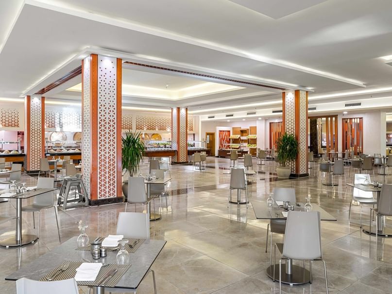 A large, modern dining area with many tables and chairs, white walls, and a shiny floor.