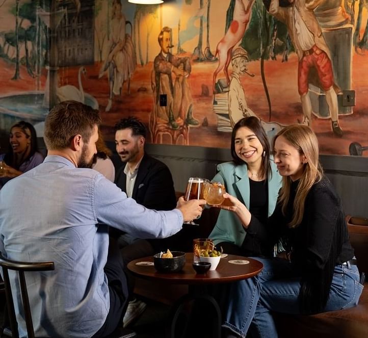 Group of friends toasting with drinks in a vibrant bar adorned with an artistic mural at The Londoner