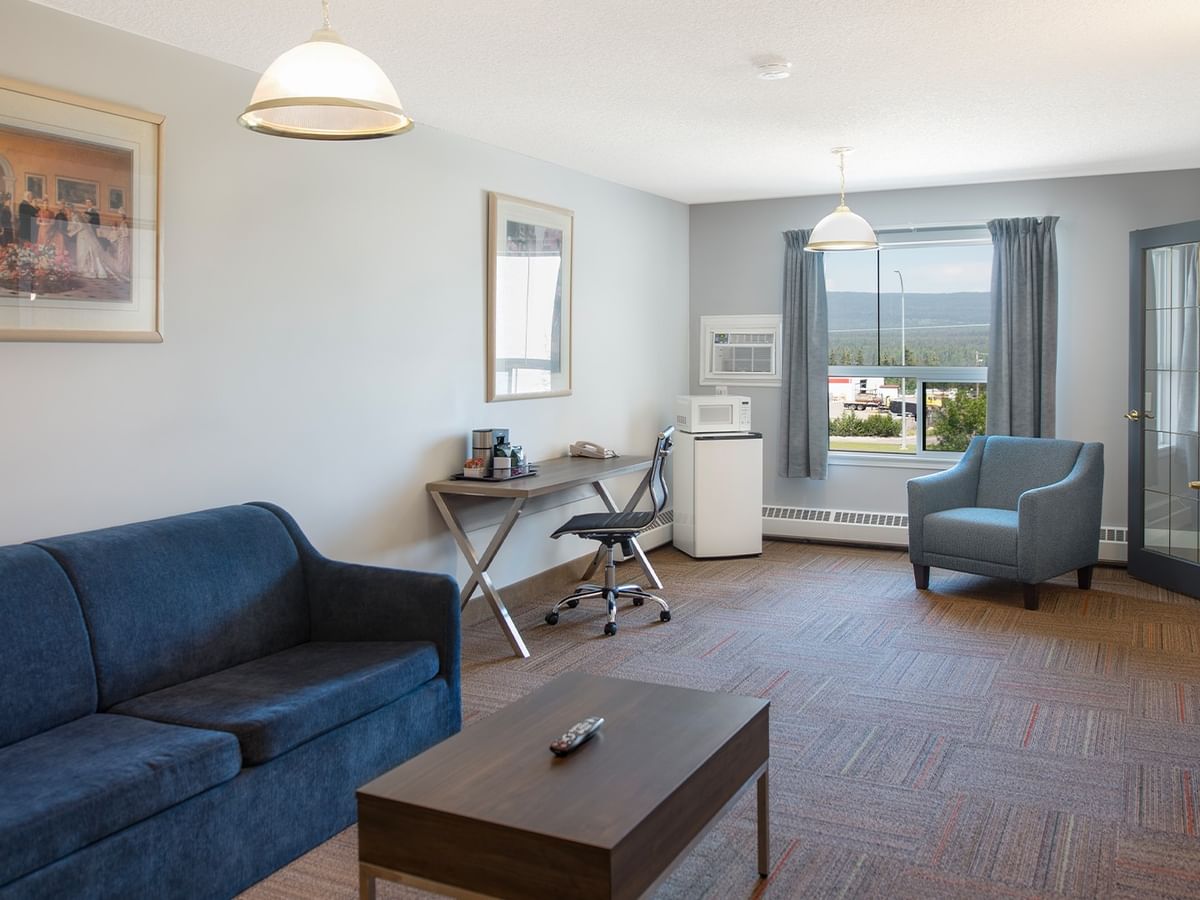 Living room with blue couch, coffee table, chair, desk, and glass door with view of buildings.