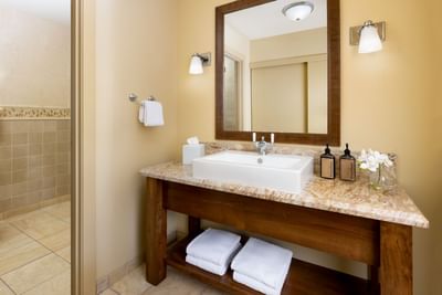 Bathroom with beige walls, wooden vanity, granite countertop, white sink, two lamps, and two towels at Elevation Resort Spa