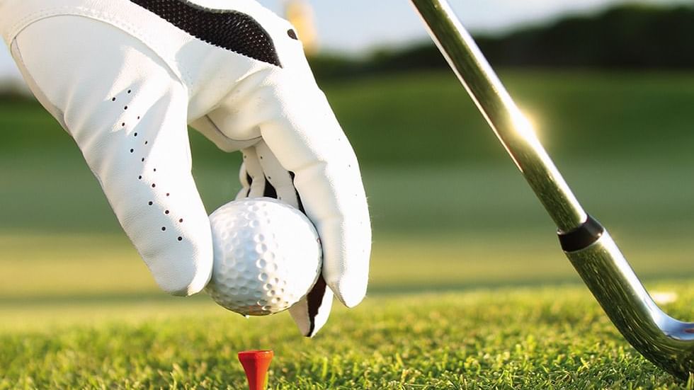 Hand wearing white gloves placing a golf ball on a red tee near Falkensteiner Hotel Belgrade