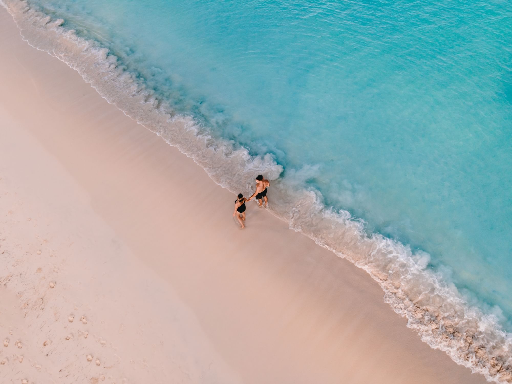 Aerial view of a couple walking along the turquoise shoreline at Amsterdam Manor Beach Resort