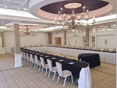 Formal U-shaped Laurel Ballroom with white chairs and tablecloths under prominent classic chandeliers at The Simsbury Inn 