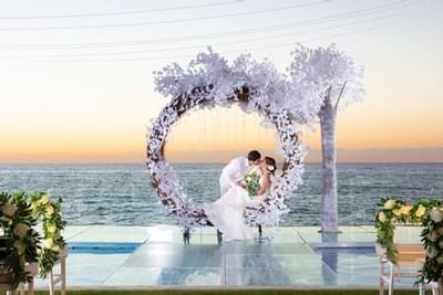 Bride and groom kissing inside a circular floral arch at sunset overlooking the ocean at Playa Los Arcos Puerto Vallarta