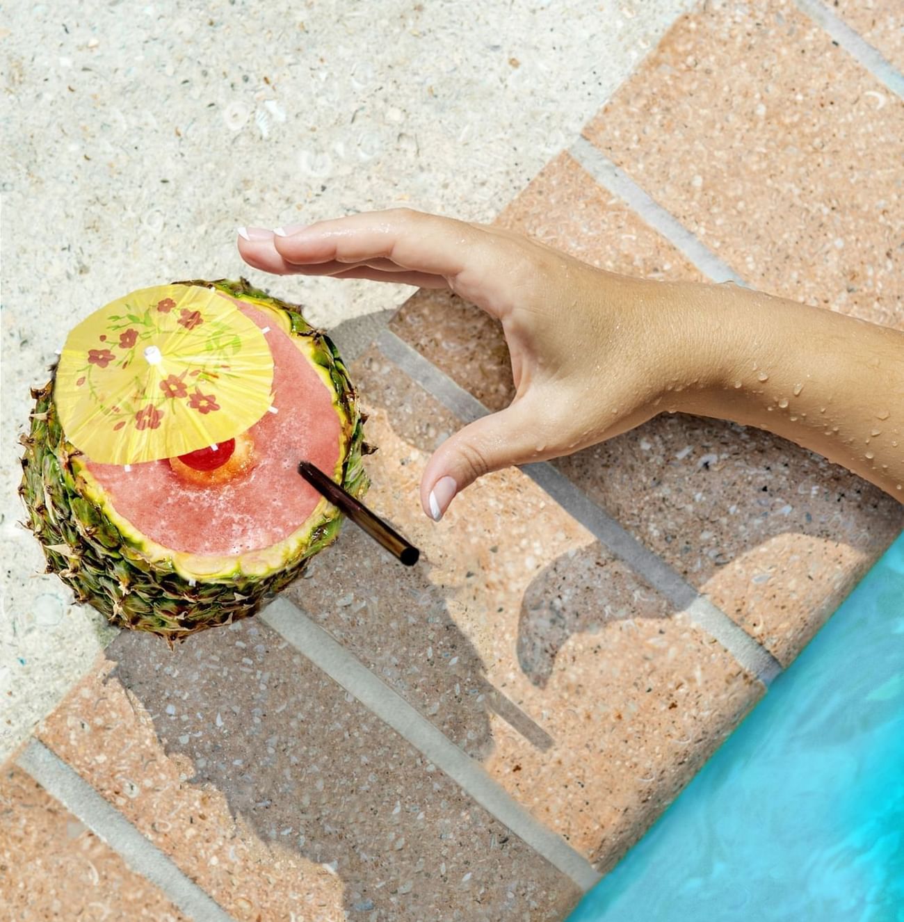 Close-up of hand reaching for a tropical drink in a pineapple by the poolside at The Grove Resort & Water Park