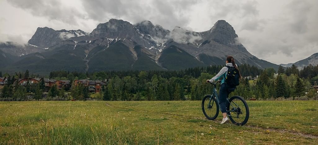 A person rides a bike while admiring the mountains in the distance in Canmore.