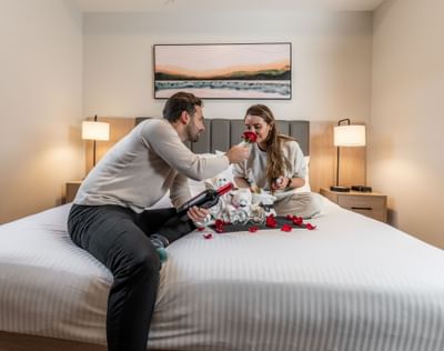 Couple sharing a romantic moment on a bed decorated with rose petals, wine, and stuffed animals at Blackstone Mountain Lodge