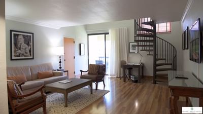 Living area with sofa and armchairs around a coffee table beside a spiral staircase in Lanai Suite at Miami Lakes Hotel