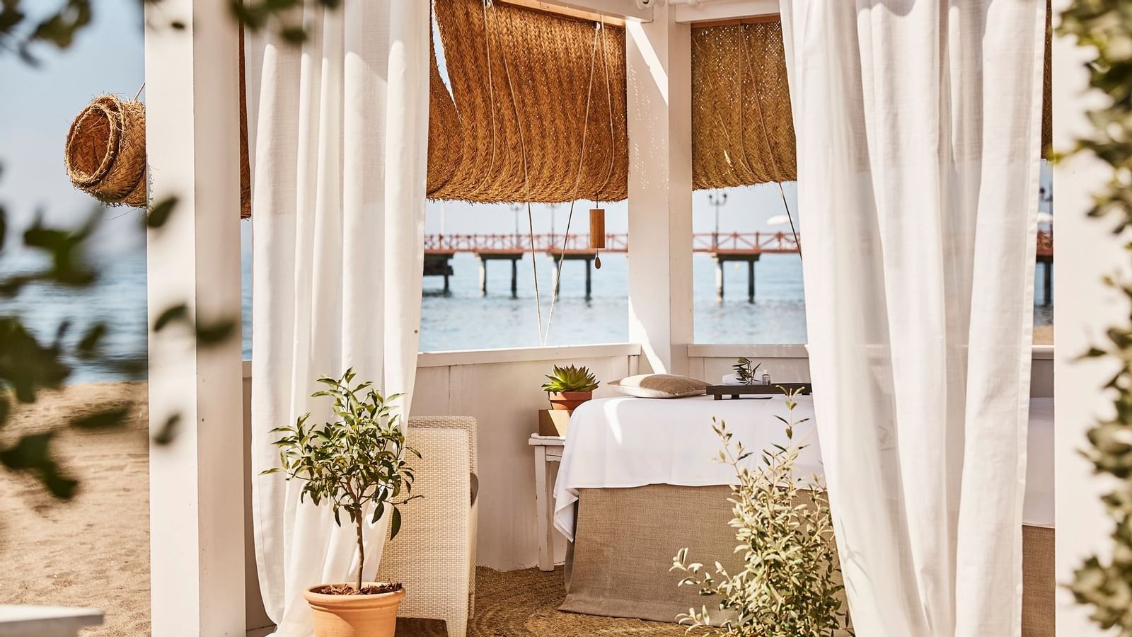 Outdoor spa treatment table placed inside a white curtained cabana, with the ocean pier visible at Marbella Club