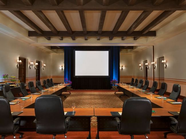 Meeting room with long tables, chairs, and a large screen in a conference room at Hacienda Del Mar Los Cabos in Cabo San Lucas.
