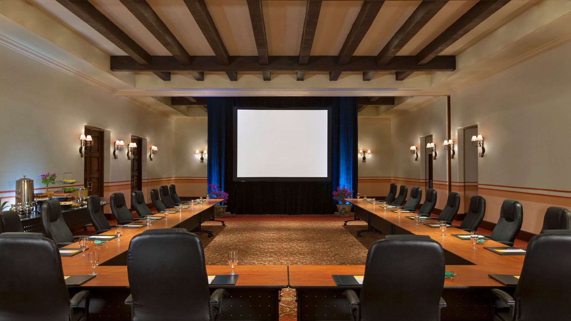 Meeting room with long tables, chairs, and a large screen in a conference room at Hacienda Del Mar Los Cabos in Cabo San Lucas.
