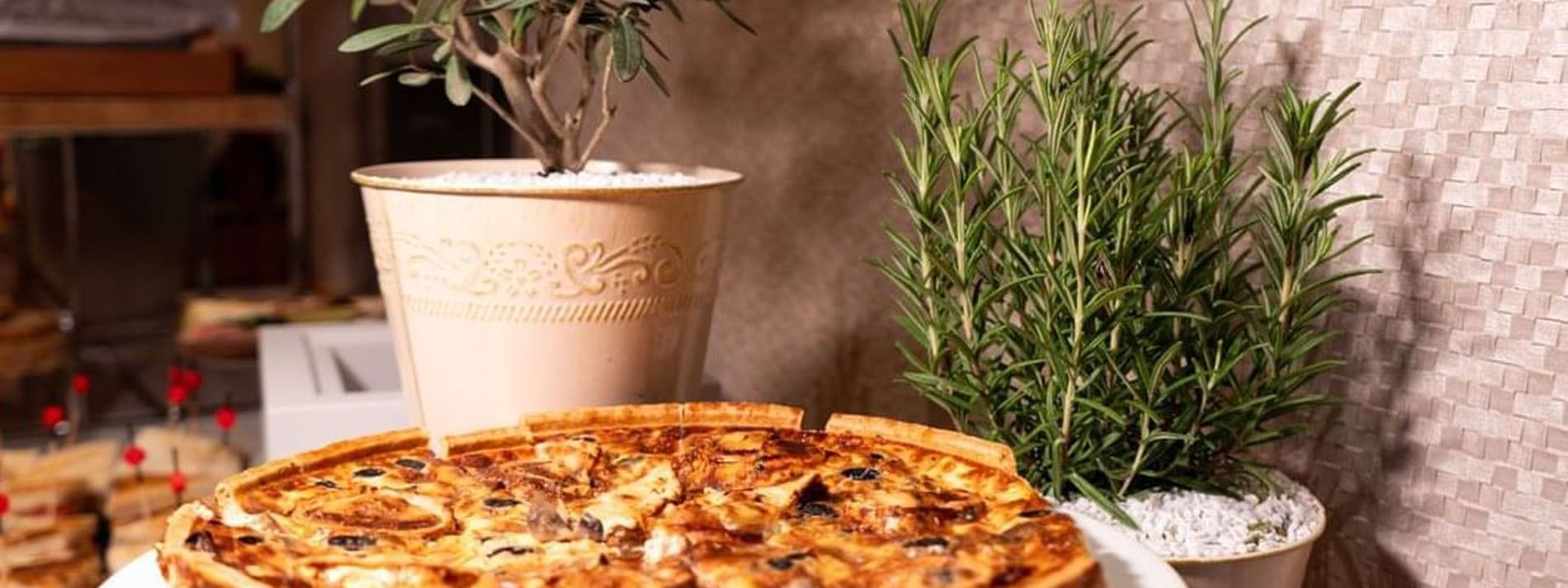 Savory quiche on a white plate by potted rosemary and olive trees in Sunday Brunch at Warwick Paris Champs Elysées