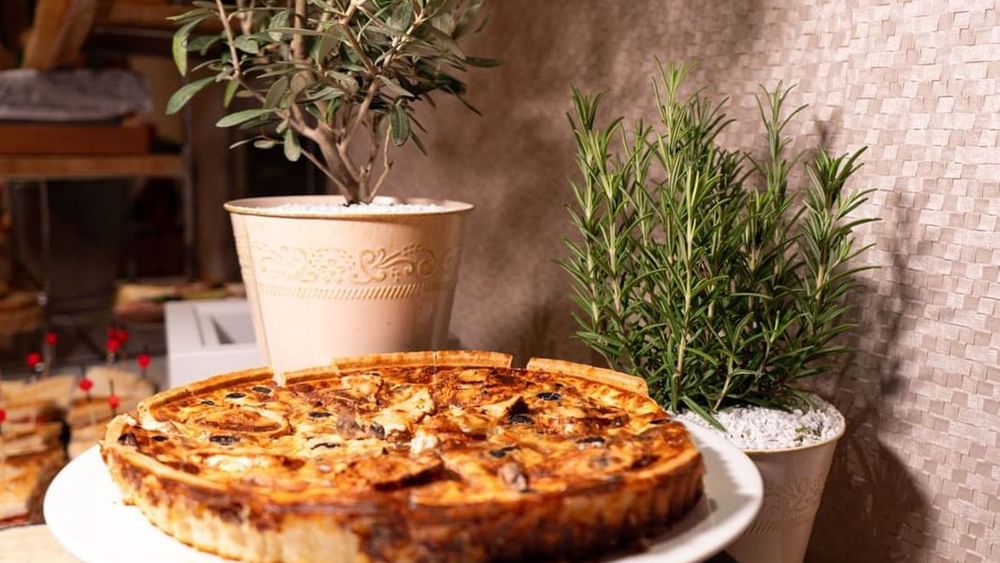 Savory quiche on a white plate by potted rosemary and olive trees in Sunday Brunch at Warwick Paris Champs Elysées