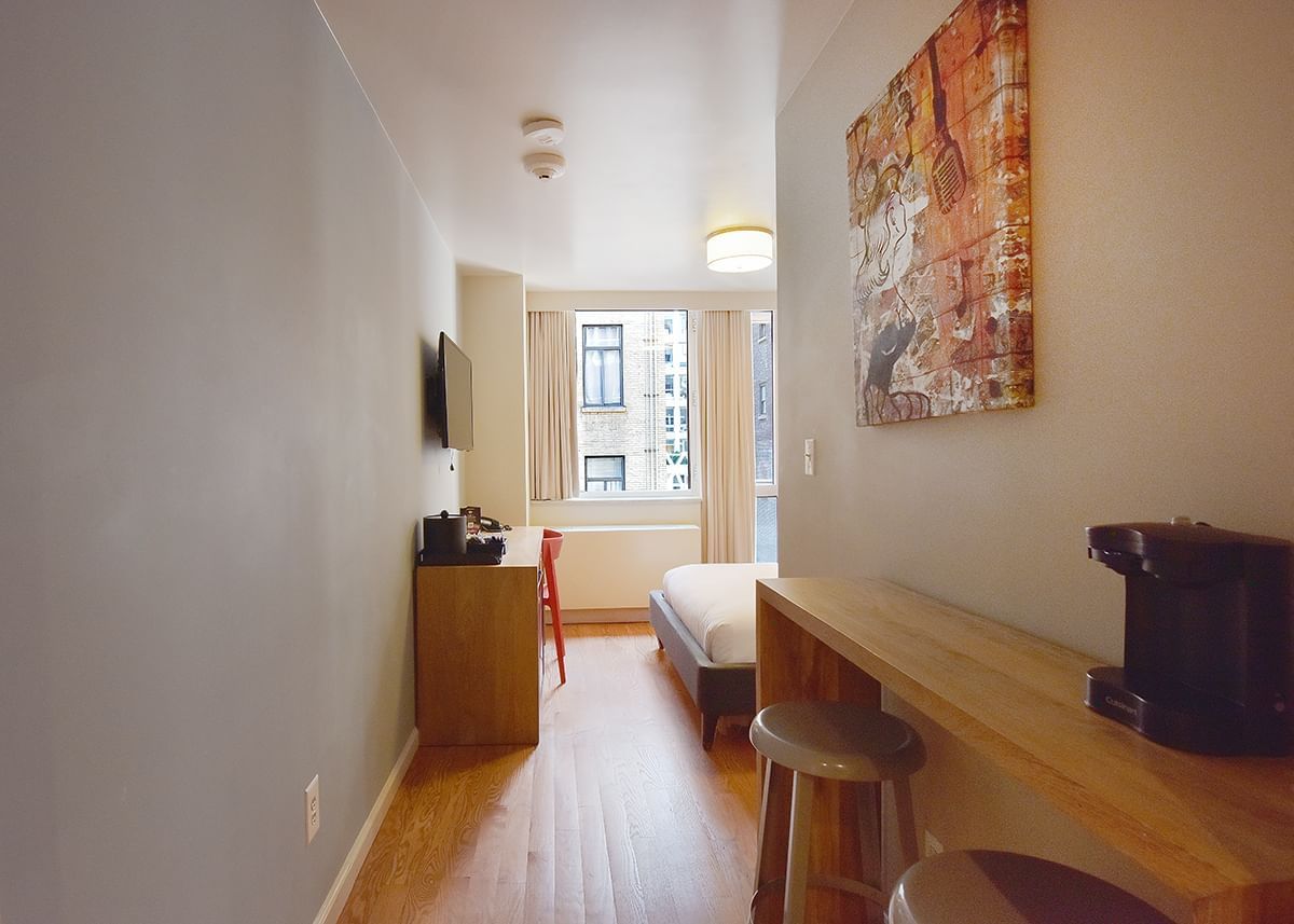 A wide view of a studio room with a sofa bed, desk, TV, and coffee maker.