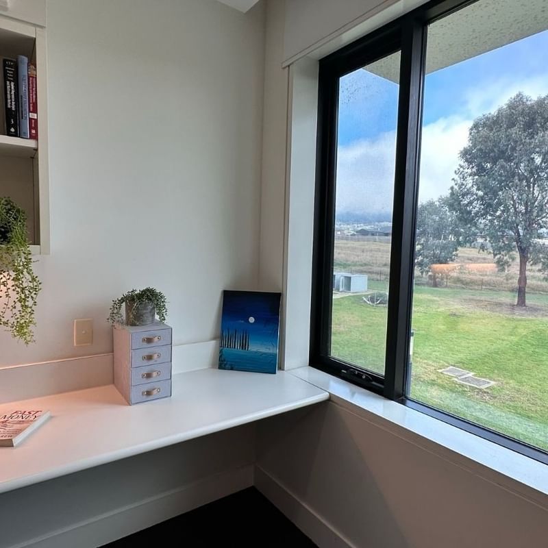 Study area with desk, books, and large window overlooking a green field.