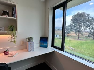 Study area with desk, books, and large window overlooking a green field.