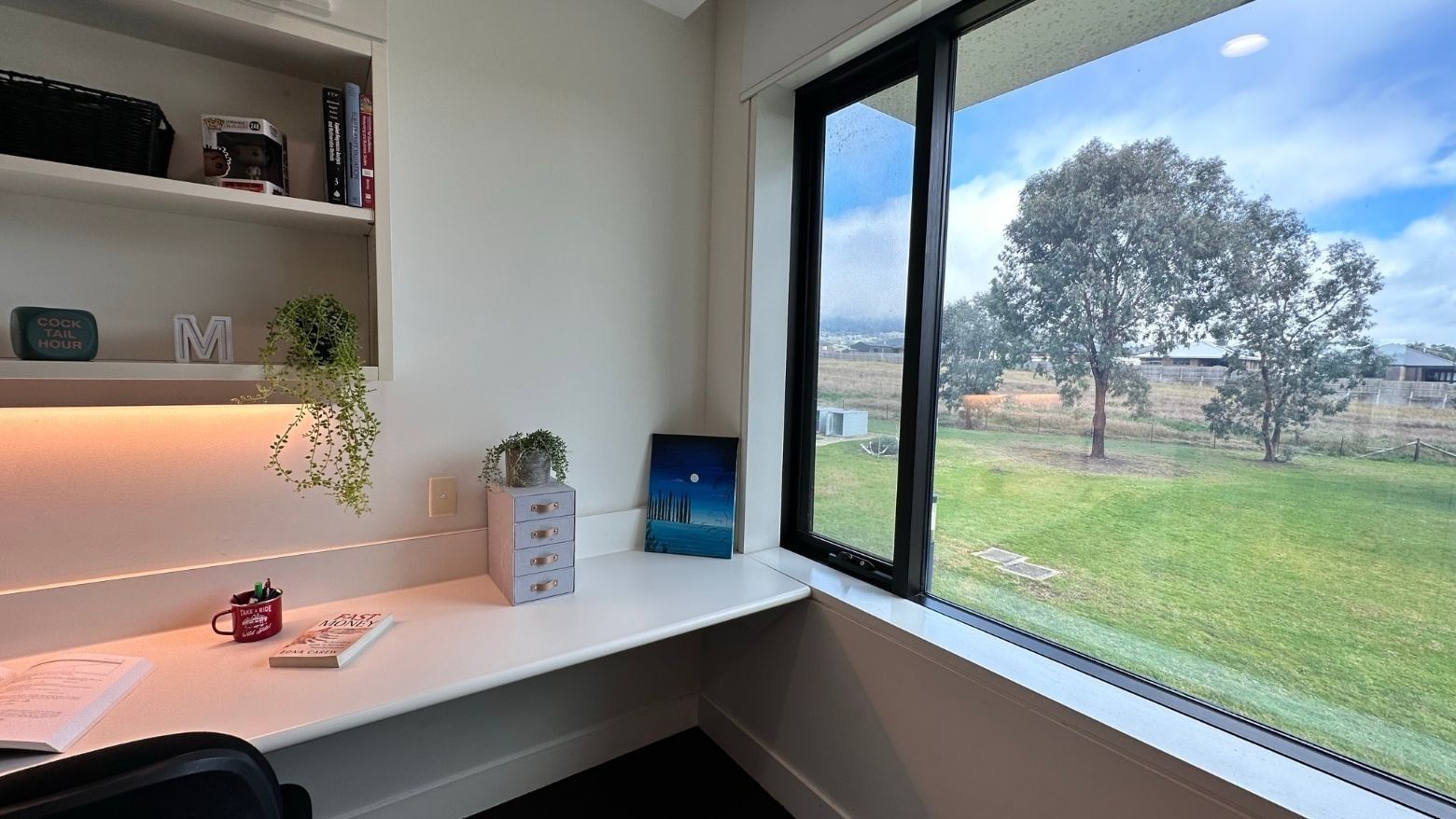 Study area with desk, books, and large window overlooking a green field.