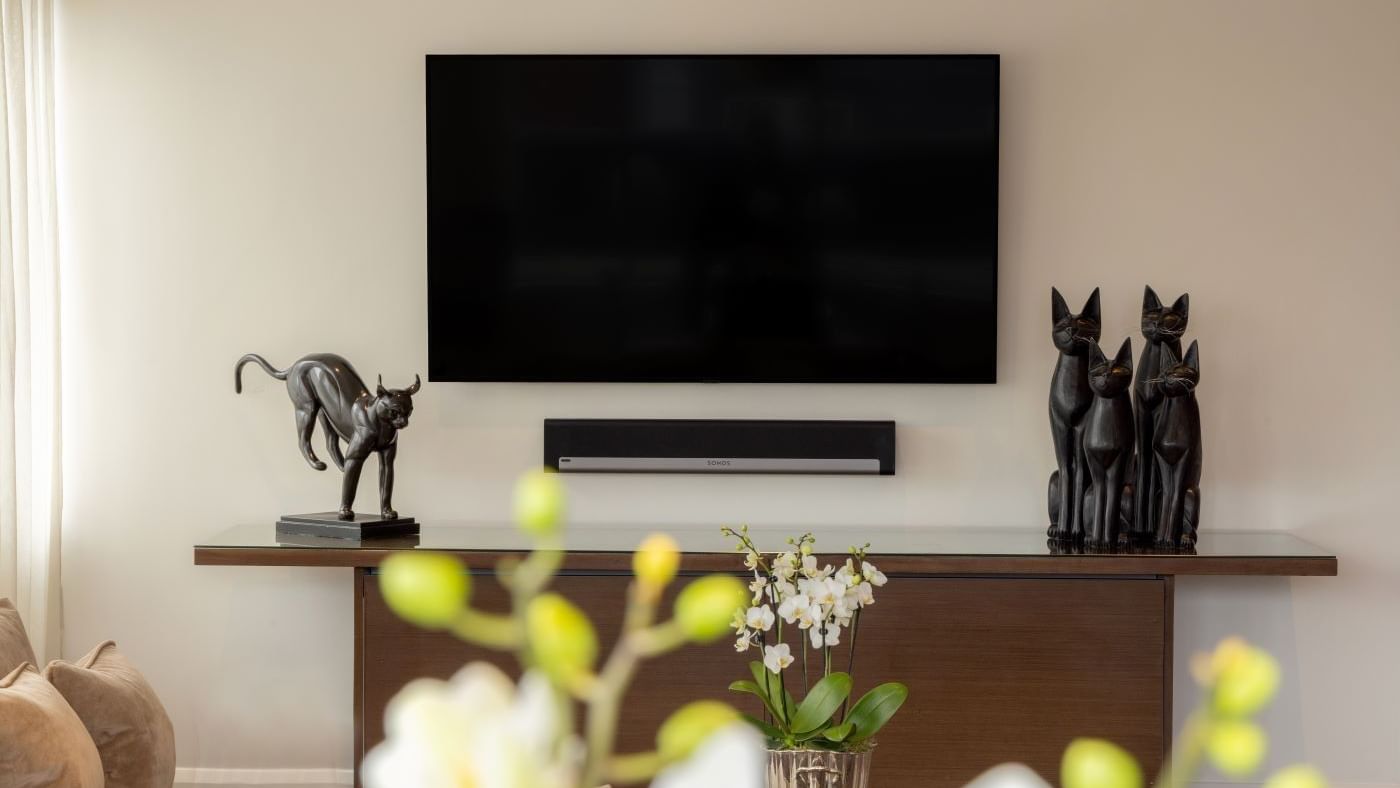 Modern living room with TV, cat sculptures, and orchids in The Saffron Suite at The May Fair Hotel, London.