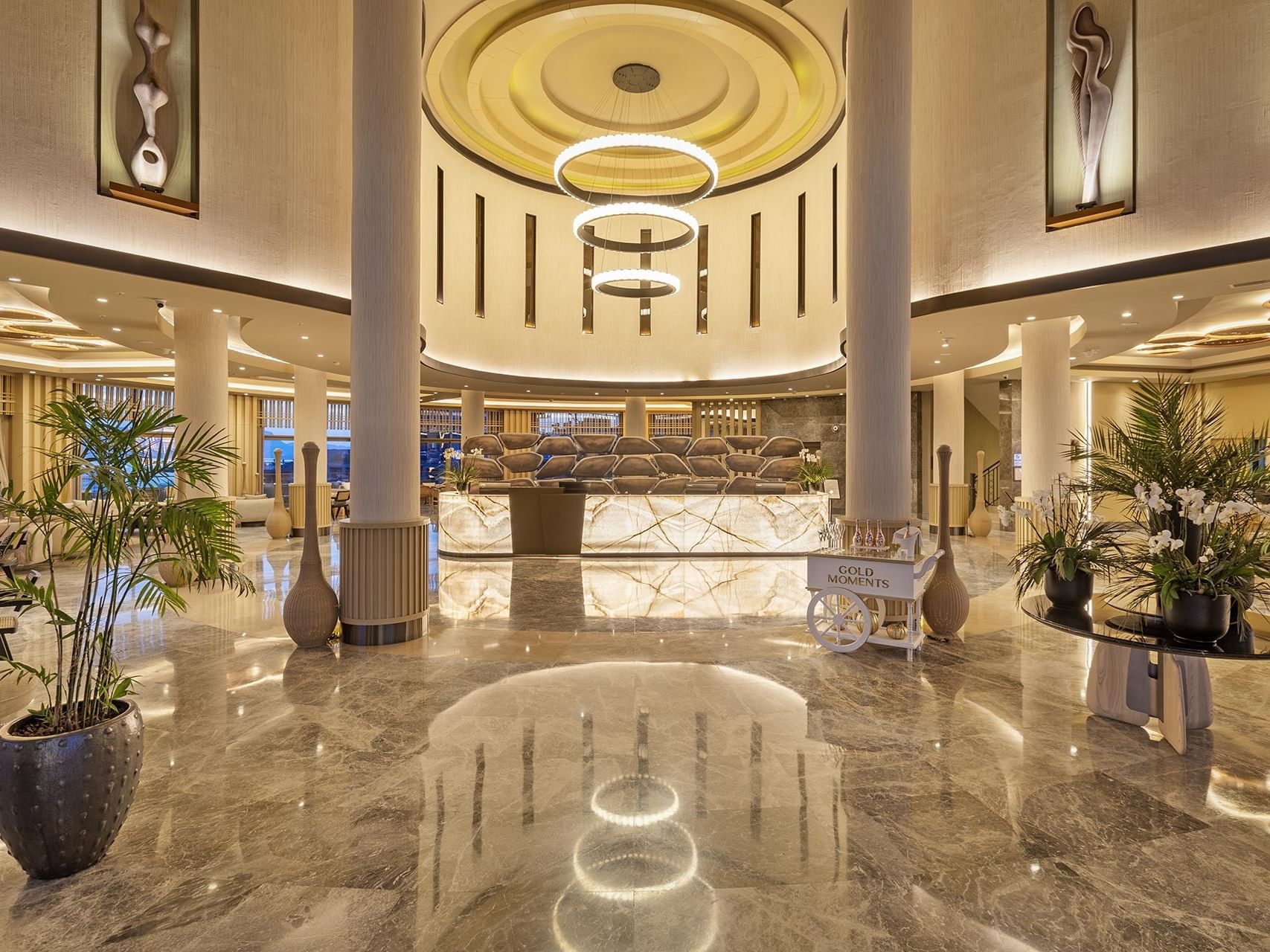Elegant lobby at Titanic Luxury Collection Bodrum featuring a circular chandelier, marble floors, and a grand reception desk.