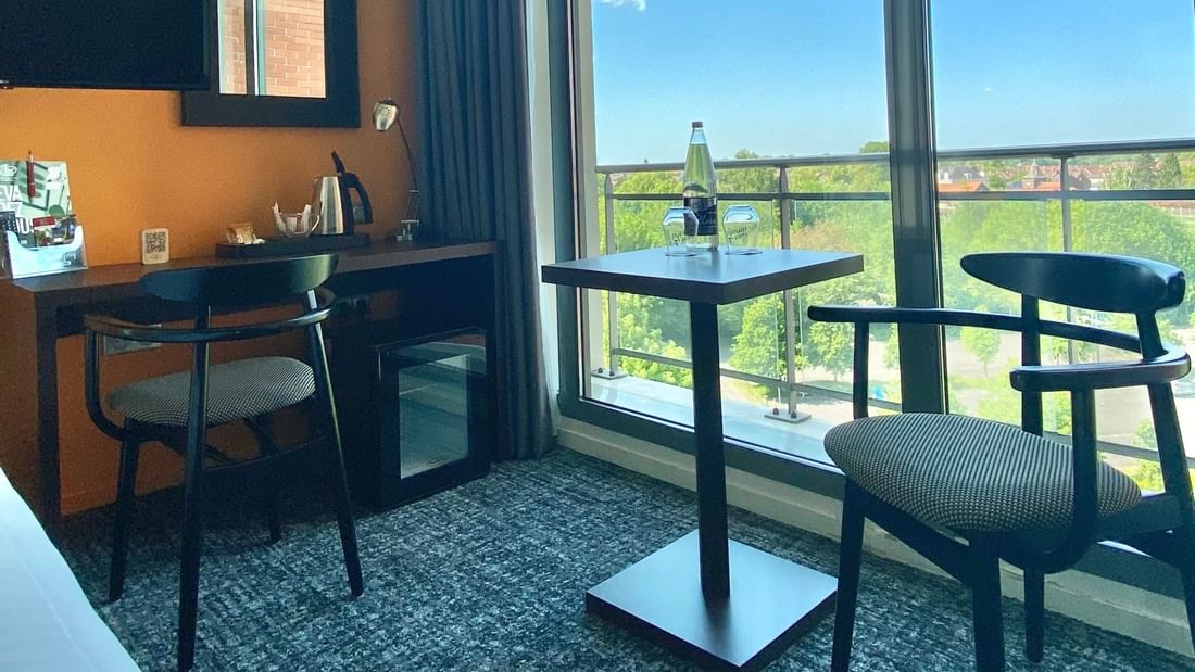 Chambre d'hôtel avec table et chaises près de grandes fenêtres offrant une vue extérieure.