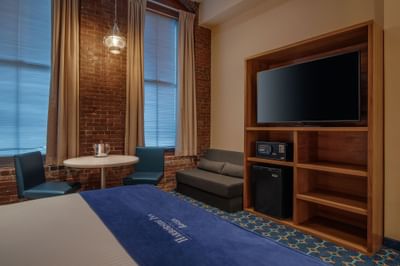 Bed near a wooden shelf unit and a table with chairs next to windows in Double Queen City View at Harborside Inn Boston