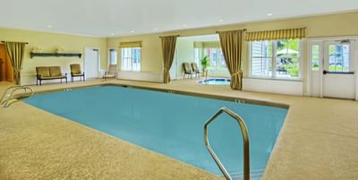 An indoor swimming pool with a connected hot tub and large windows at The Pointe at Castle Hill