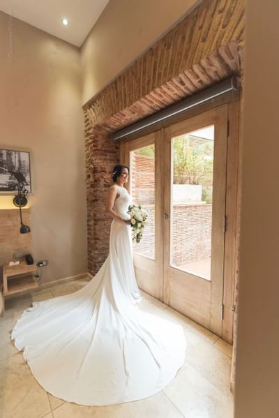 Bride standing elegantly by wooden doors, holding a bouquet at Billini Hotel Historic Luxury