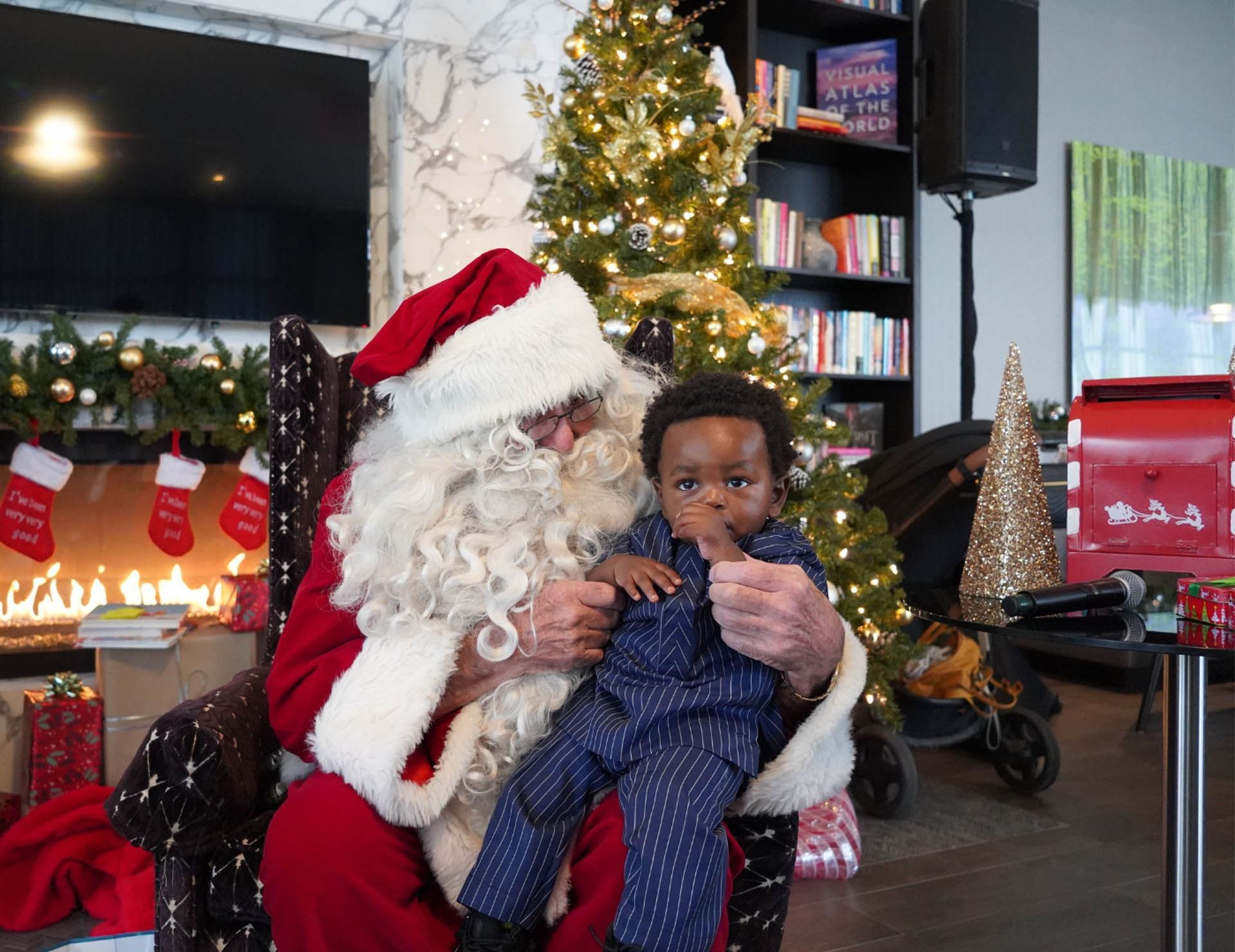 Santa Claus holding a toddler beside decorated Christmas tree and warm fireplace during festive event at Hotel X Toronto