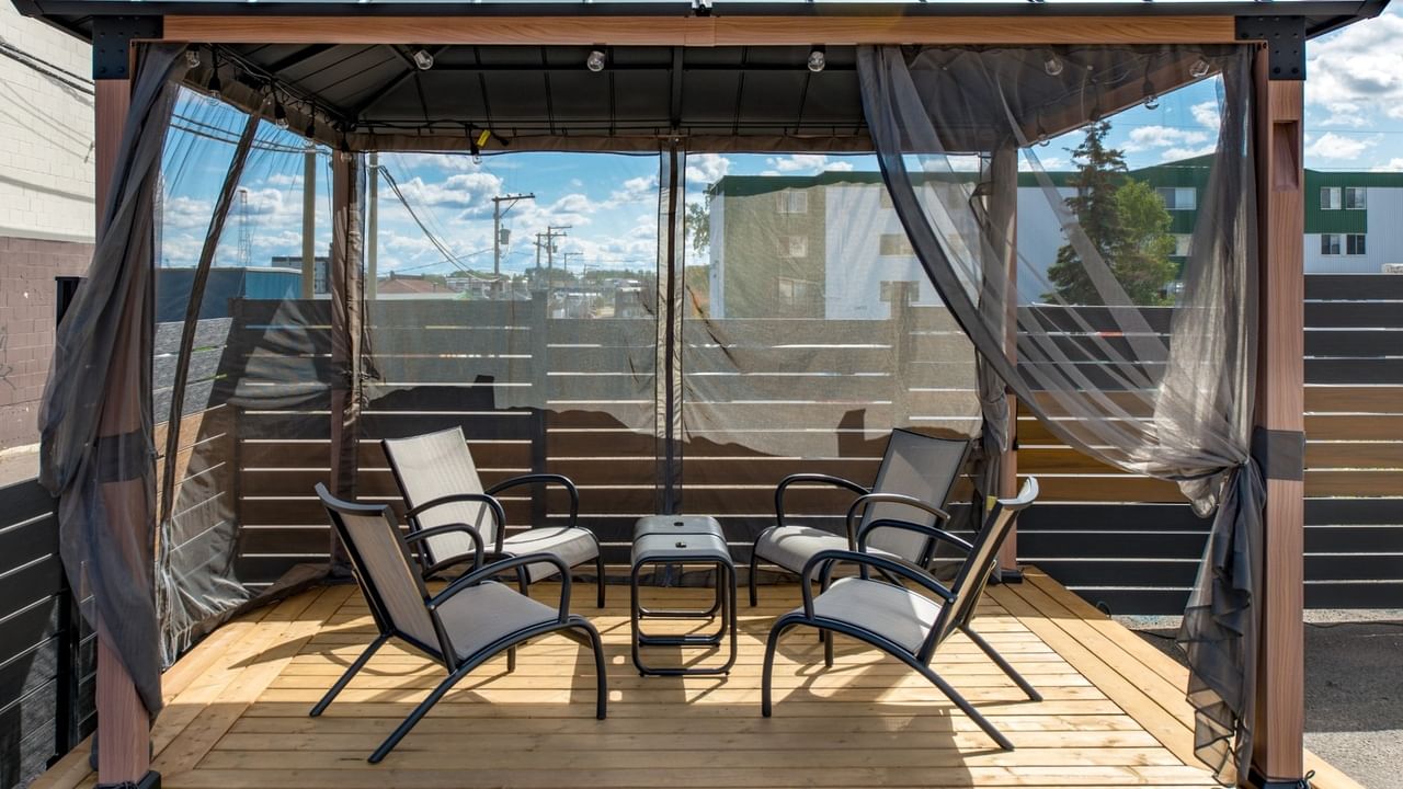 Cabana with chairs and a table under a canopy with mesh curtains on a wooden deck.