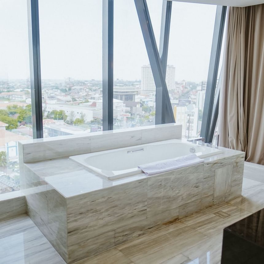 Bathtub with a city view in a room with marble floors at Po Hotel Semarang