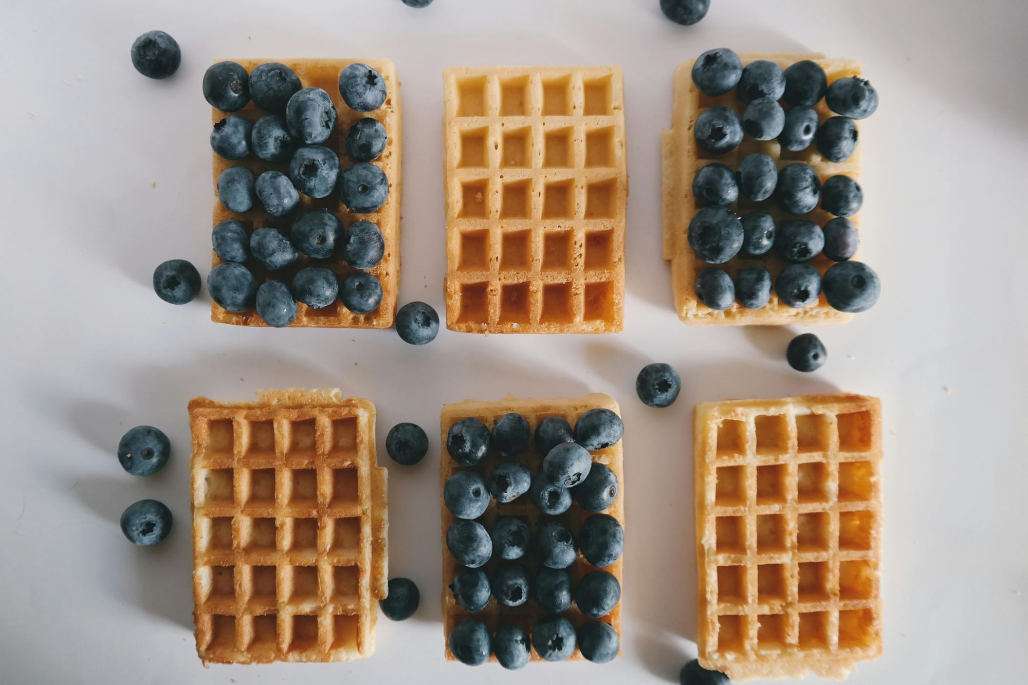 Image of six of the best waffles in Orlando against a white background, three of which are dressed in blueberries for National Waffle Week.