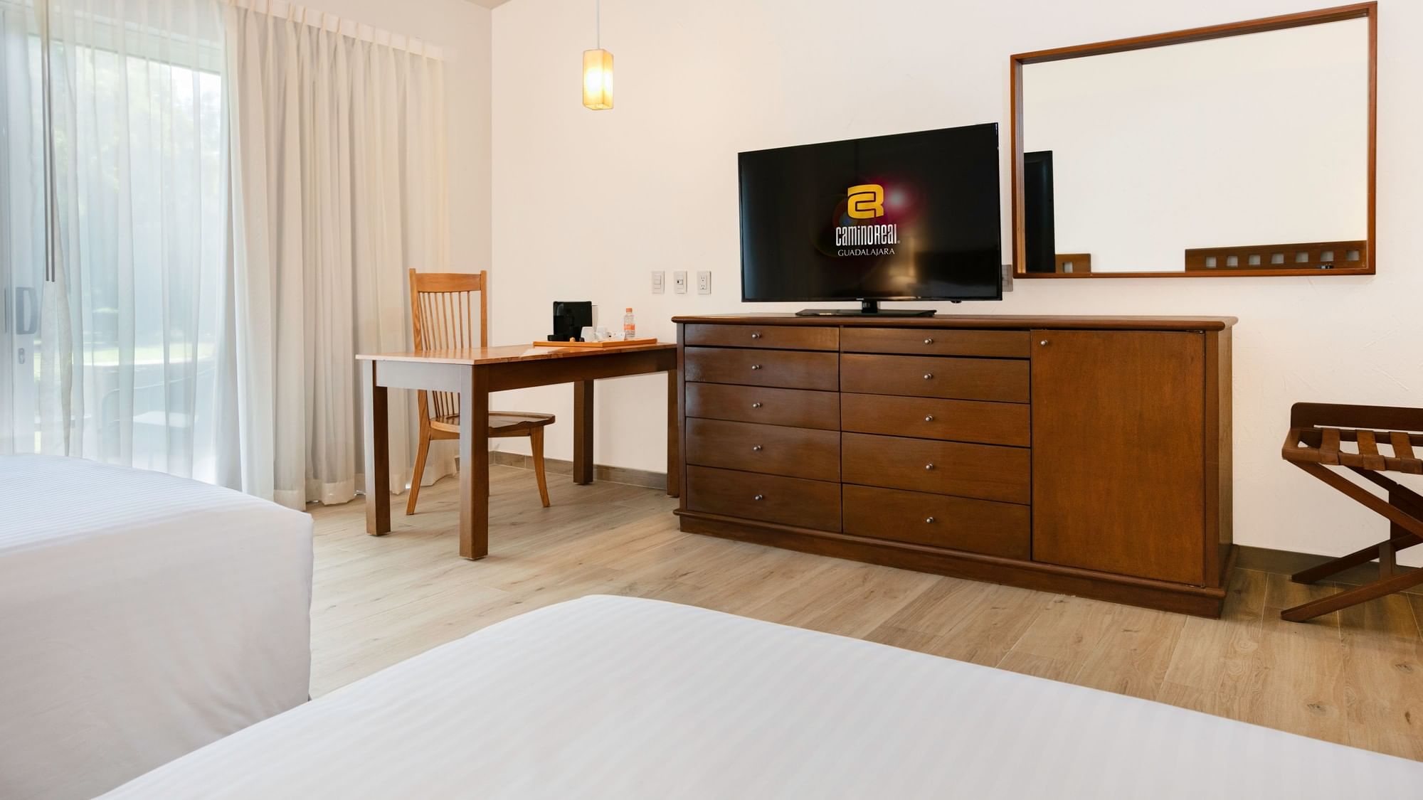 Two beds, a desk, and a dresser with a TV at Camino Real Guadalajara in Zapopan