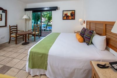 Hotel room with large bed, chairs, table, sliding glass doors to balcony, and a view of a pool.