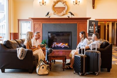 Four guests with luggage relaxing on brown leather sofas by the warm fireplace at Rodd Crowbush Golf & Beach Resort