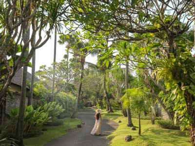 Woman in hat and dress walking along tree-lined pathway at Peppers Seminyak