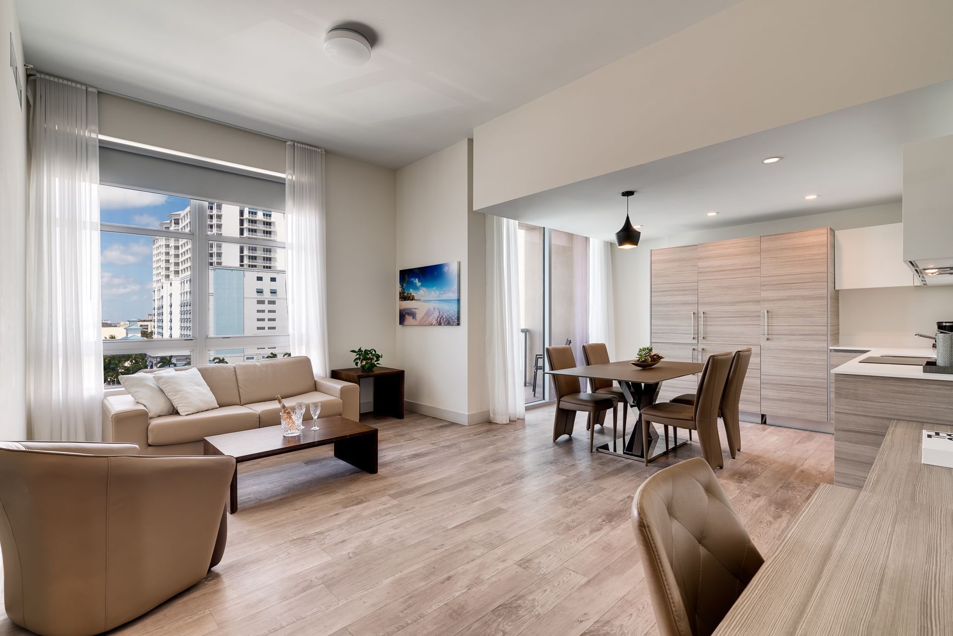 A wide view of a modern living room and kitchen area with a dining table, sofa, and city view.