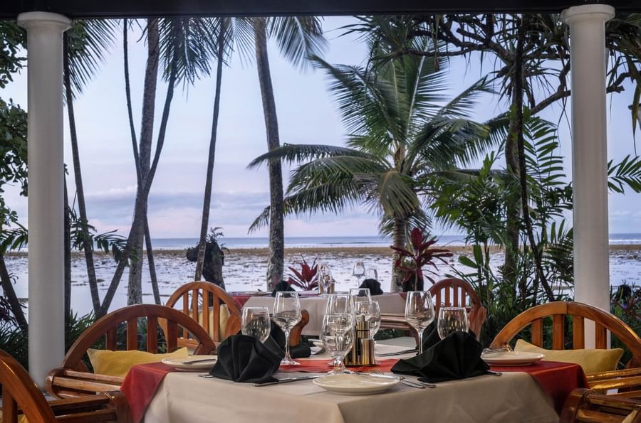 Set table with wine glasses by palm trees near the ocean in Pappagallo at Warwick Fiji Resort and Spa