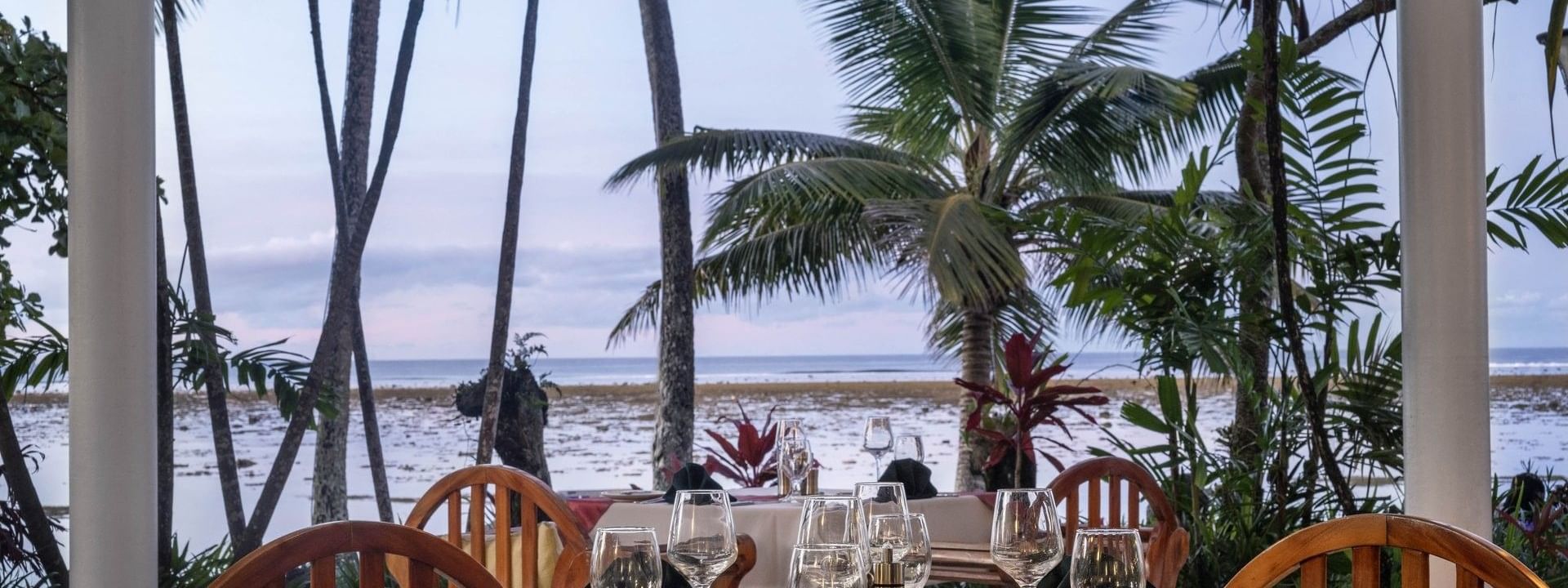 Set table with wine glasses by palm trees near the ocean in Pappagallo at Warwick Fiji Resort and Spa