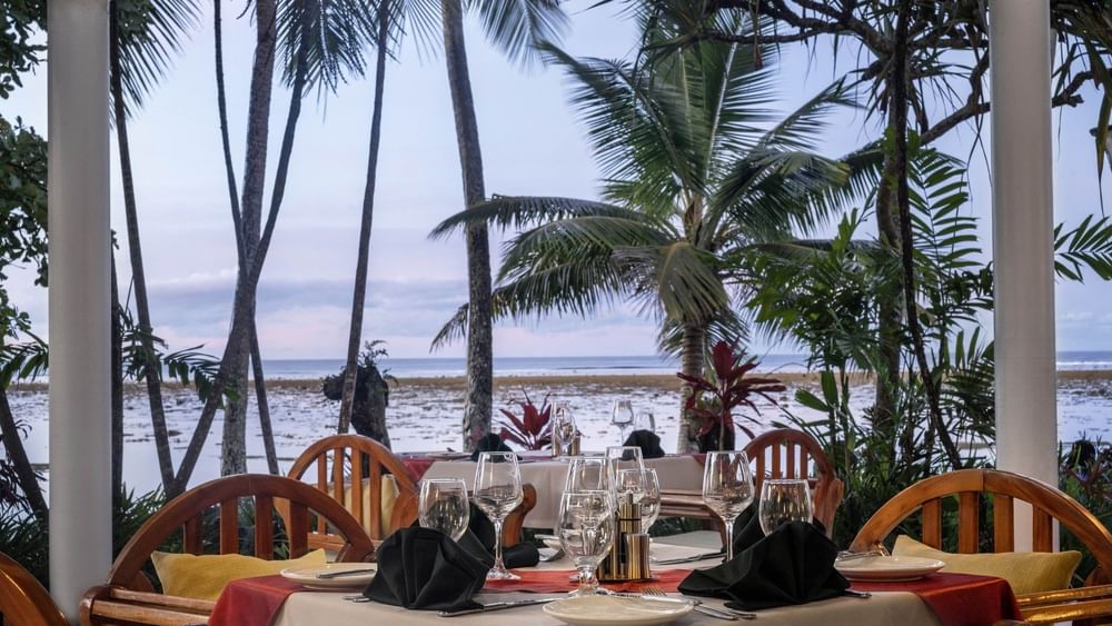 Set table with wine glasses by palm trees near the ocean in Pappagallo at Warwick Fiji Resort and Spa
